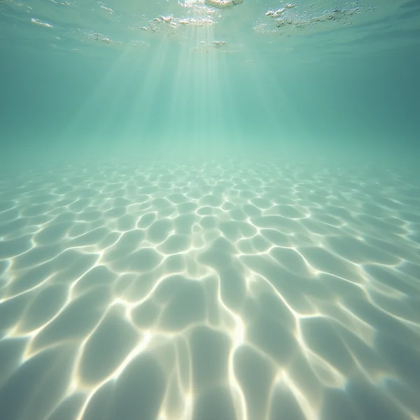 Sunlight caustics rippling across a pale sandy seabed seen from underwater, shafts of light descending from the surface above