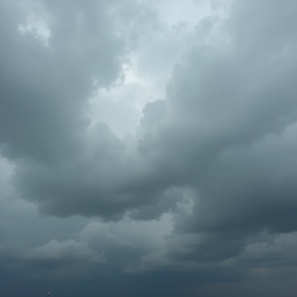 A heavy bank of layered grey storm cloud filling the frame, its folds lit unevenly from behind