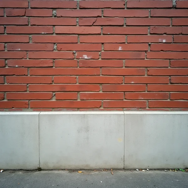 A red brick wall above a pale concrete plinth, with pavement running along the base