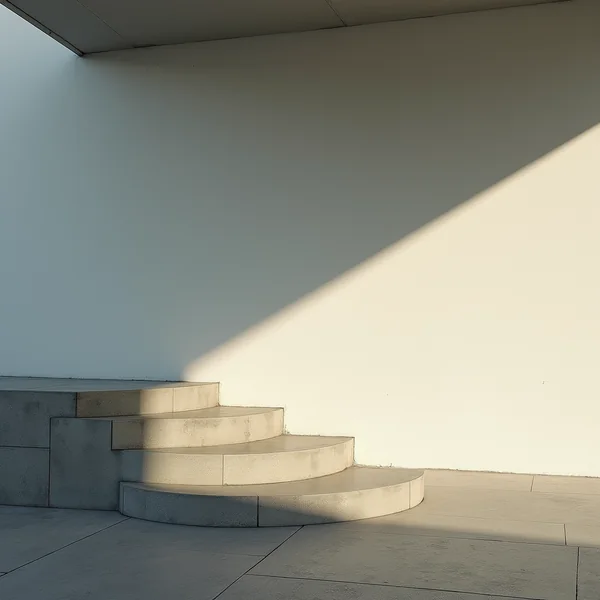 Curved concrete steps beside a plain wall, with a diagonal band of low sunlight across it