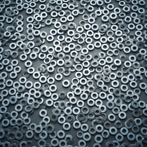 Hundreds of galvanised steel washers of varying diameters scattered in a single layer across a dark surface