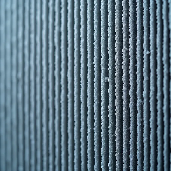 A dense row of thin vertical grey-blue metal heat exchanger fins filling the frame, pale frost gathered along their ridges, sharp through the centre and falling out of focus toward the left edge