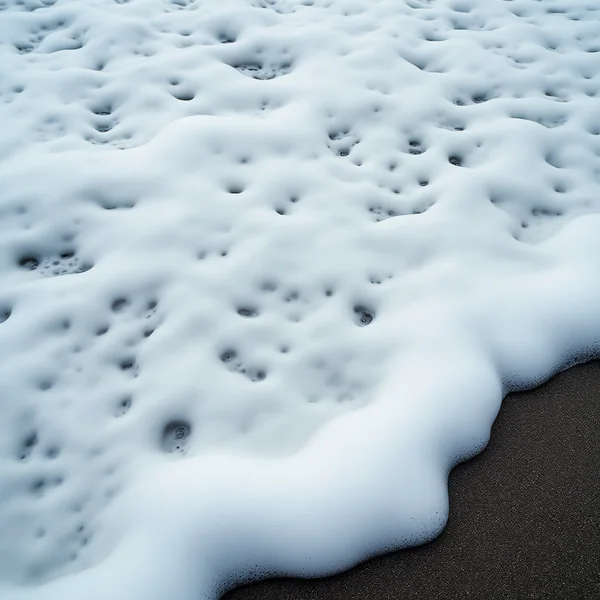 Dense white sea foam of thick clustered bubbles breaking over dark wet sand