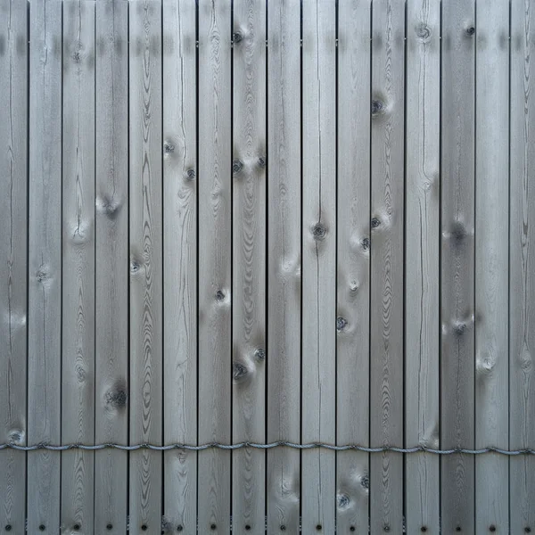 A weathered wooden slat fence of close silvered vertical boards bound with a twisted wire